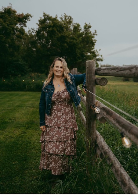 Danielle Baril standing by a wooden fence in a green field
