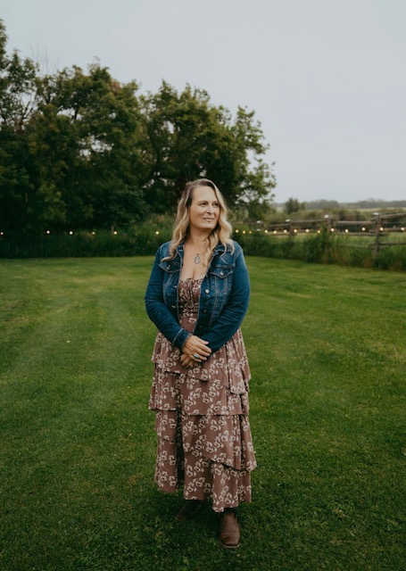 Danielle Baril standing in an open field at dusk with string lights behind her